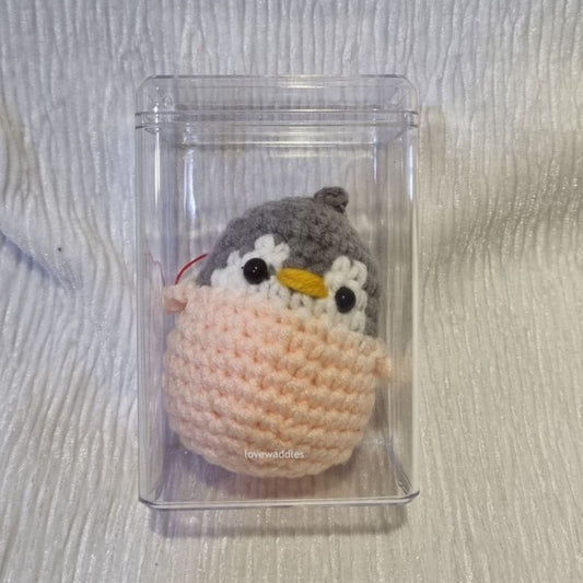 A crochet penguin inside an acrylic box. 